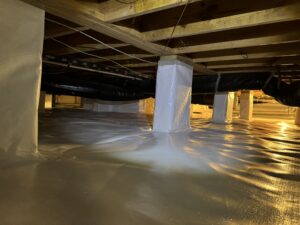 A crawl space with a clean white vapor barrier covering the ground and support columns, and black ductwork visible overhead.