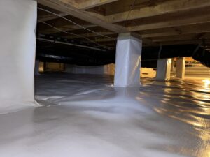 A clean and well-maintained crawl space with white vapor barrier lining the floor and walls, exposed wooden beams overhead, and ventilation ductwork visible.