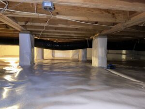 A clean, insulated crawl space with wooden beams, plastic sheeting on the ground, and wrapped support pillars. Wires and a duct run along the ceiling.