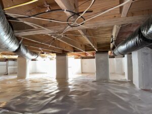 A crawl space with wooden beams, insulated ducts, and a white vapor barrier on the floor and columns.