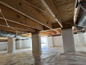 A crawl space with exposed wood beams, insulation, and ductwork. The floor and some columns are covered with a white vapor barrier.