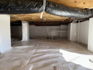 A clean, well-lit crawl space with a sealed floor and insulated ducts visible above. There is a white bench and an electrical outlet with a cord plugged in near the center.