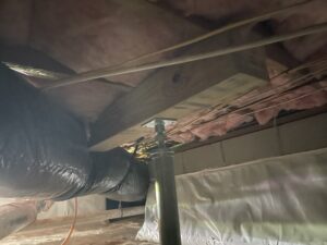 A basement ceiling with exposed insulation, ductwork, and a metal jack supporting a wooden beam.